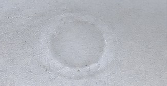 A faint ring on a white TPO membrane where hail struck over a fastener plate