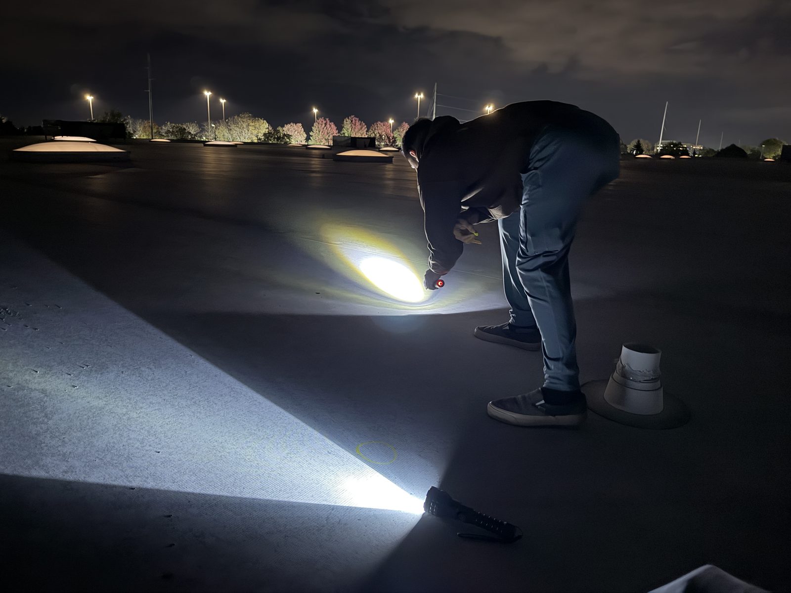 Our team inspecting a flat roof at night with flashlights held low to the membrane