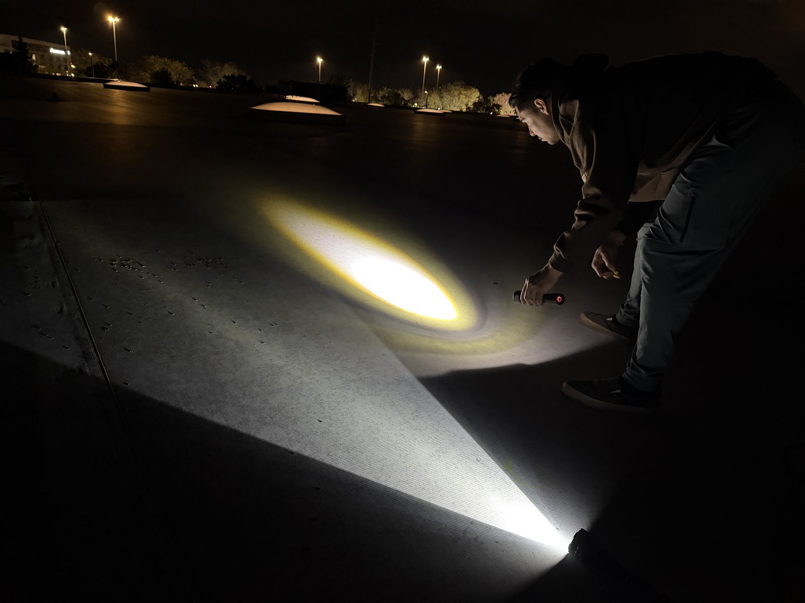 Flashlight beam raking across a flat roof at night, showing shadows in hail dents